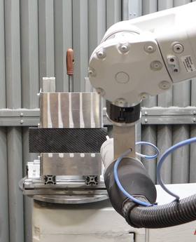Robotarm naast het composiet-metaalproefstuk in de coldspray-opstelling van Windesheim.